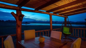 A wooden deck with a table and chairs, overlooking a body of water and distant mountains. - Soetdoring Selfsorg (Oudtshoorn)
