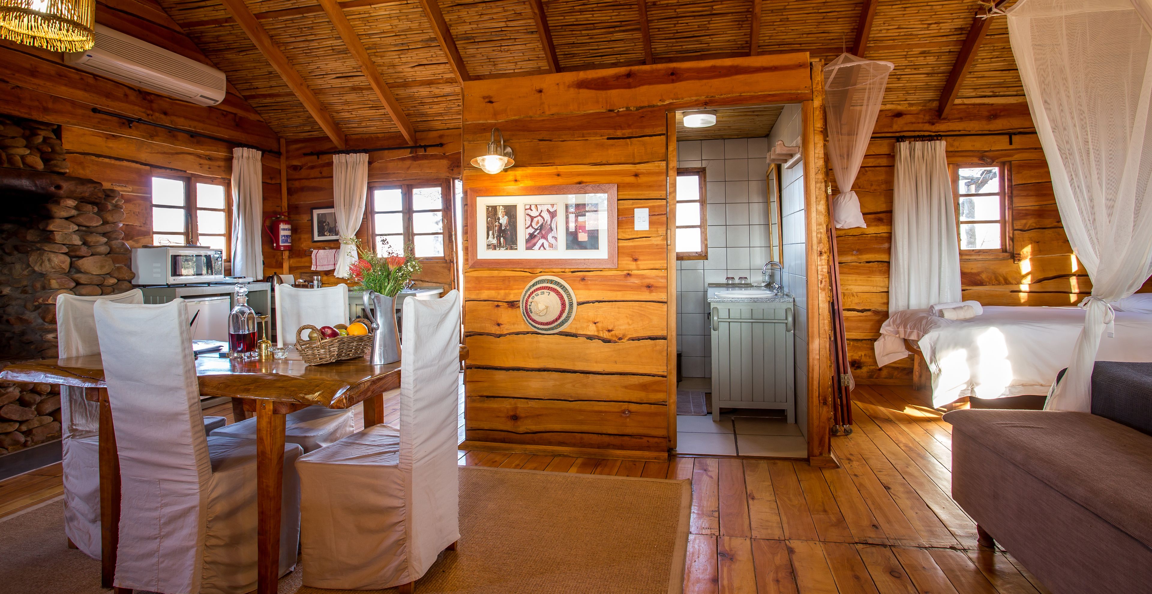 A wooden cabin with a dining area, kitchenette, and a bedroom with a bed and canopy.