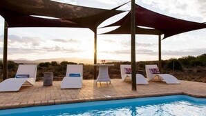 A poolside area with lounge chairs and umbrellas, a pool, and a view of the landscape. - Soetdoring Selfsorg (Oudtshoorn)