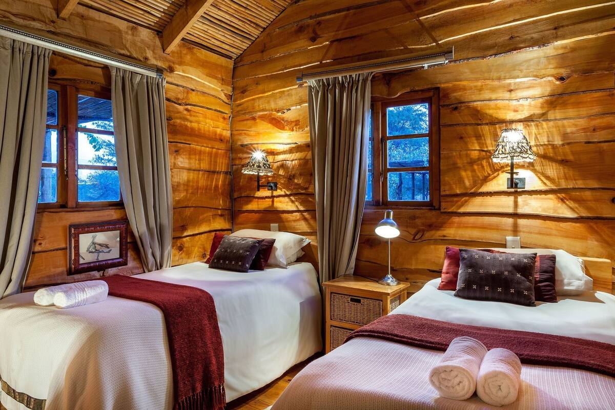 Habitación de cabaña de madera con dos camas, un cuadro enmarcado y una lámpara.