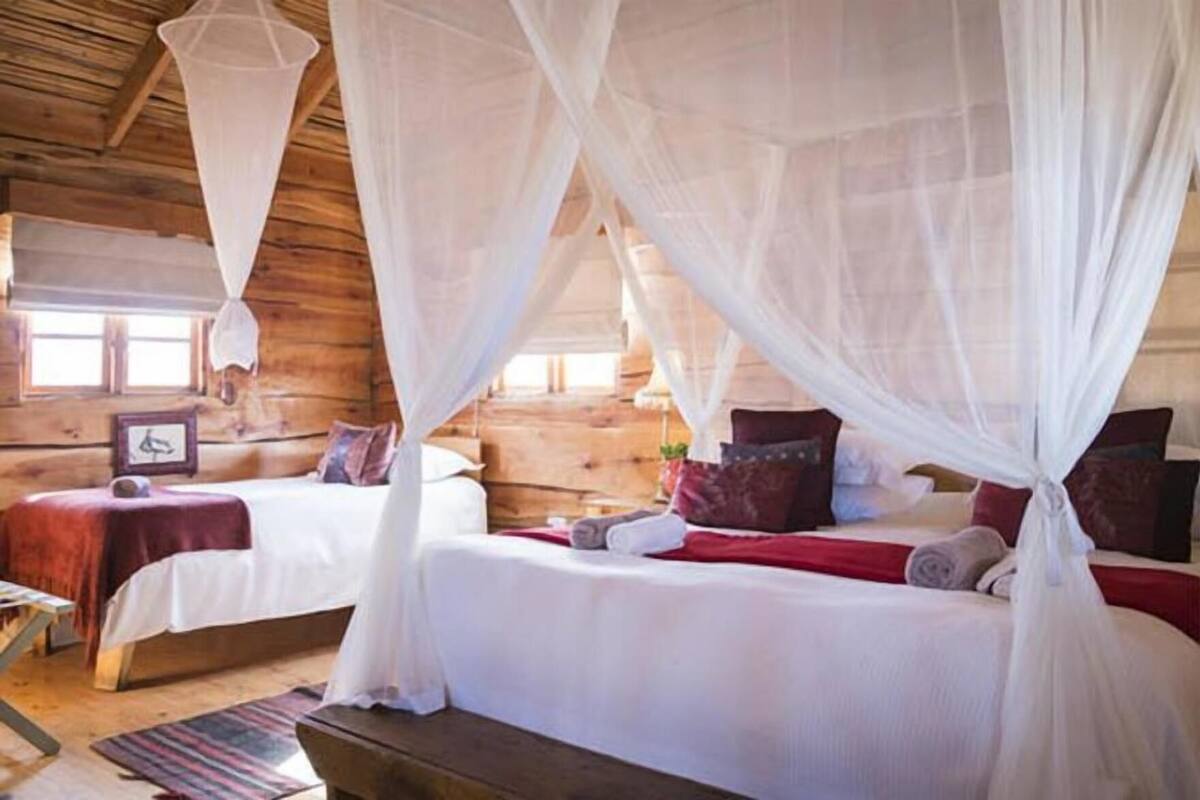 Habitación con dos camas, cada una con dosel, paredes de madera y una mesita con una silla.