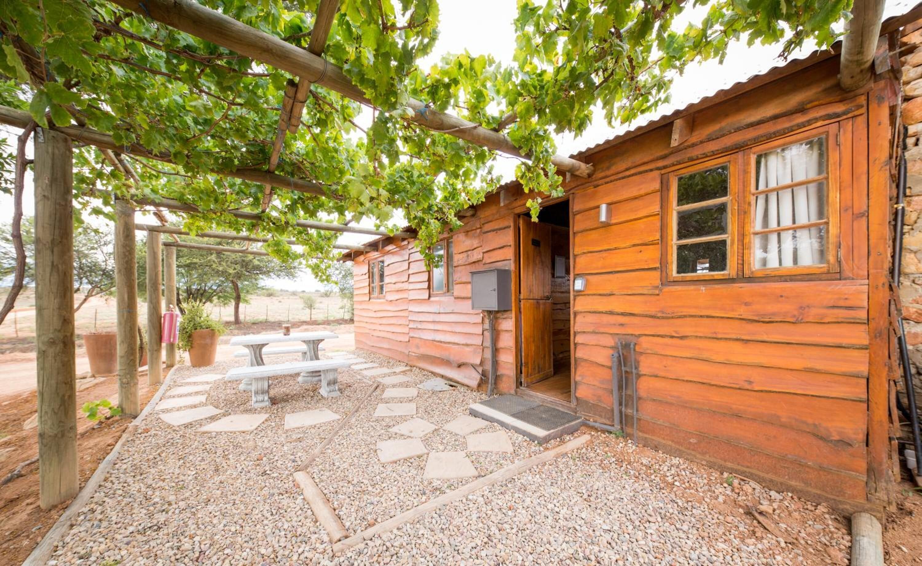 Una cabaña de madera rústica con un patio de grava, un pérgola de madera y una mesa de picnic.