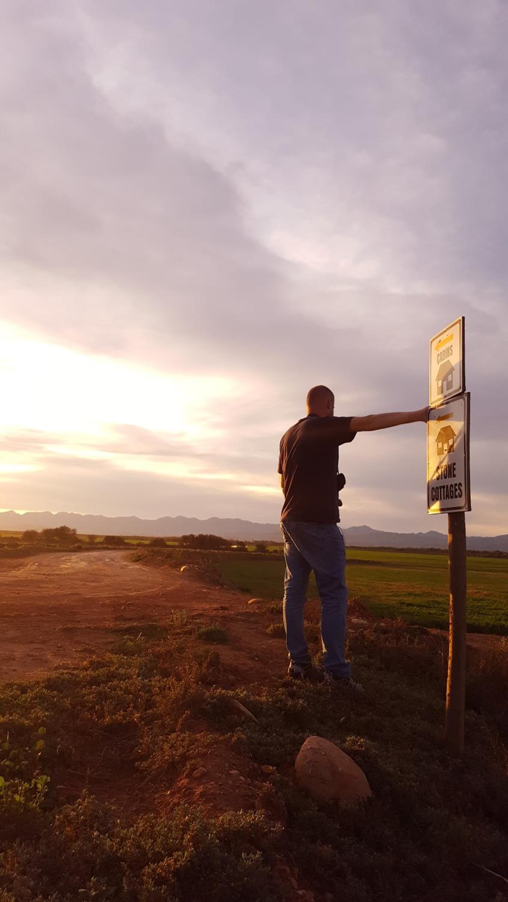 A person pointing at a signpost with 'CABINS' and 'STONE COTTAGES' labels.