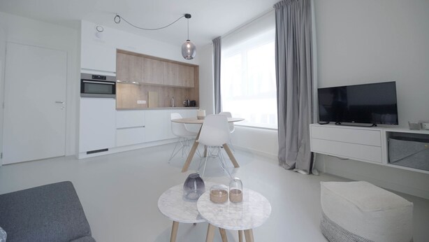 A modern living room with a grey sofa, a small round table with two candles, and a TV on a white stand. - Florence en Ville (Brussels)