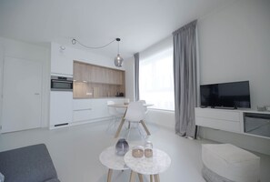 A modern living room with a grey sofa, a small round table with two candles, and a TV on a white stand. - Florence en Ville (Brussels)