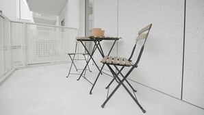 A balcony with a white metal fence, a small table with a chair, and a potted plant. - Florence en Ville (Brussels)