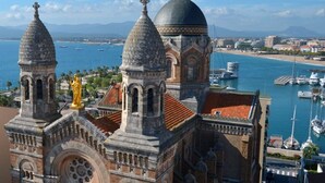 Un edificio histórico con torres abovedadas y una gran cúpula central, que domina un puerto deportivo con barcos.