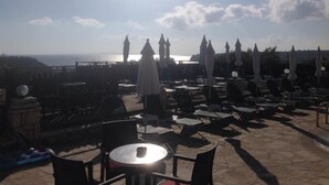 A rooftop terrace with sun loungers and umbrellas, overlooking a body of water. - Ariadne Apartments (Zakynthos)