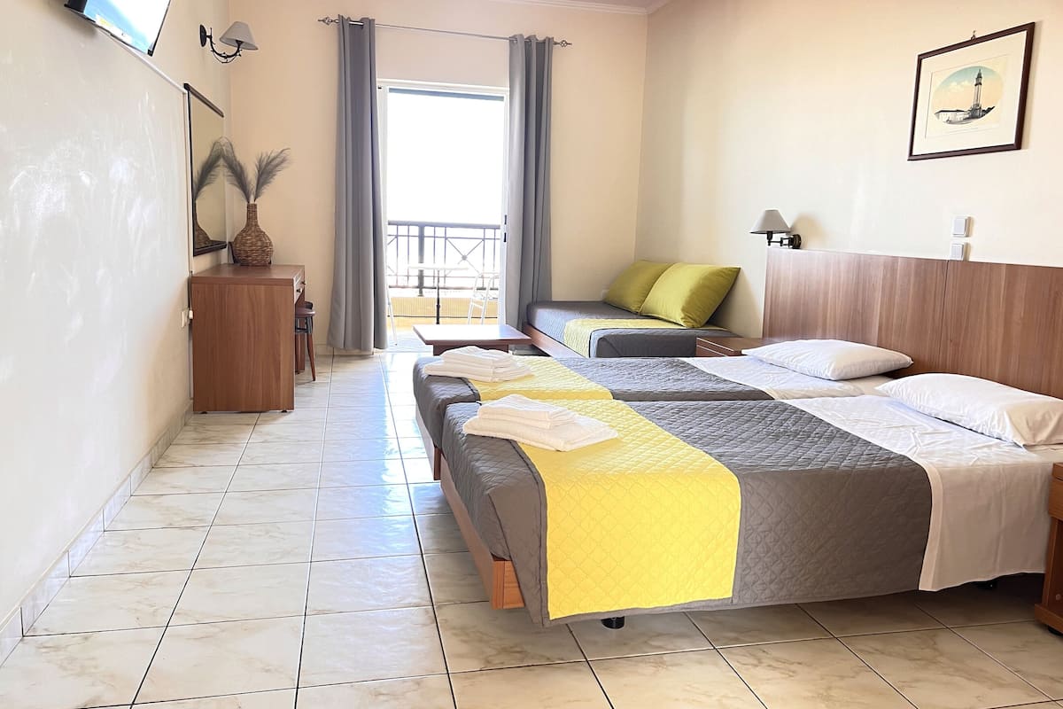 A hotel room with two beds, a desk, a chair, a TV, and a balcony with a view.