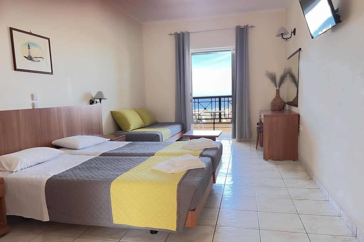 A hotel room with two beds, a small table, a chair, a balcony with a view, and a TV mounted on the wall.