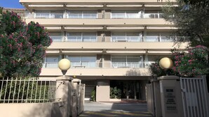 A multi-story building with a beige facade, balconies on each floor, and a gated entrance.