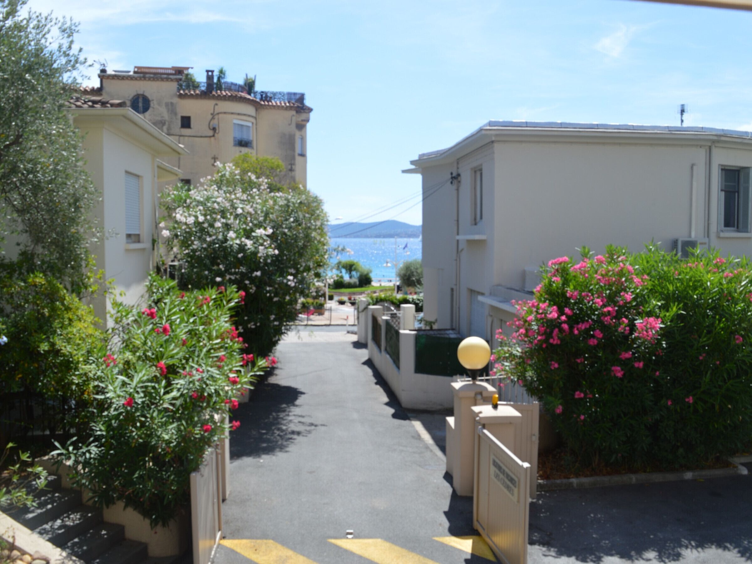 Eine schmale Straße mit Gebäuden an beiden Seiten, ein Tor mit einem gelben Pfeil und in der Ferne ein klarer Blick auf das Meer und die Berge.