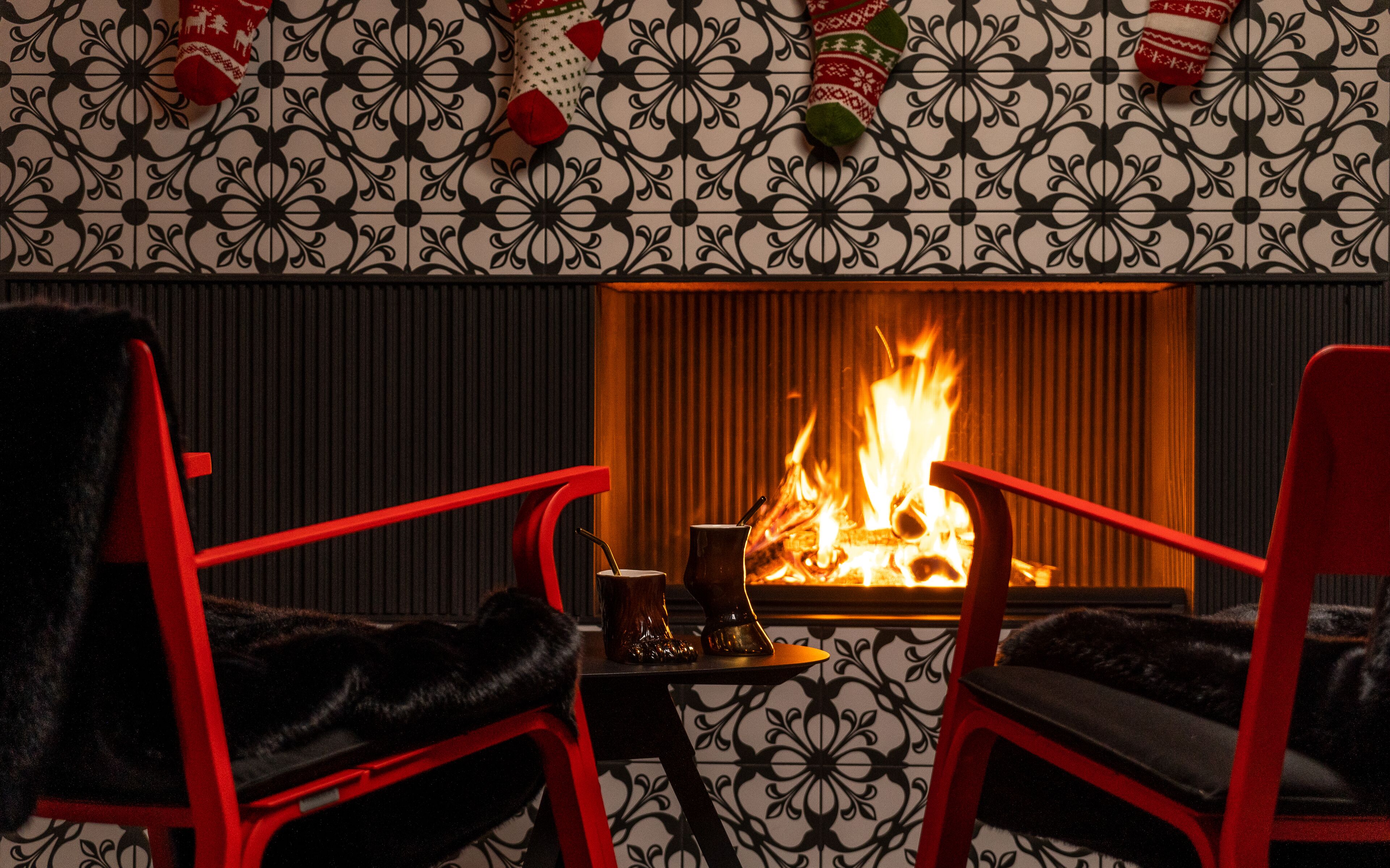 A room with a fireplace, two red chairs, and patterned wallpaper.