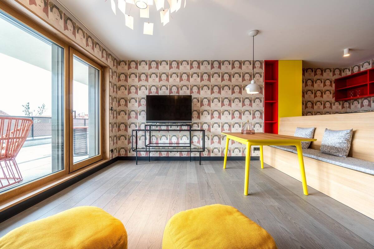 Un salon moderne avec une grande fenêtre, un téléviseur, une table jaune et une étagère rouge.