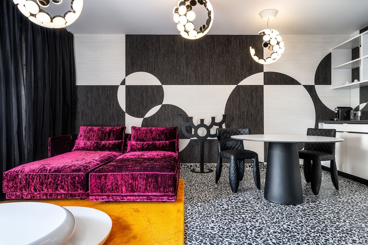 Un salon moderne avec un canapé rose vif, une table de salle à manger ronde et un coin cuisine doté de meubles blancs.