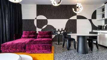 Ein modernes Wohnzimmer mit einem leuchtend rosafarbenen Sofa, einem runden Esstisch und einer Küchenzeile mit weißen Schränken.