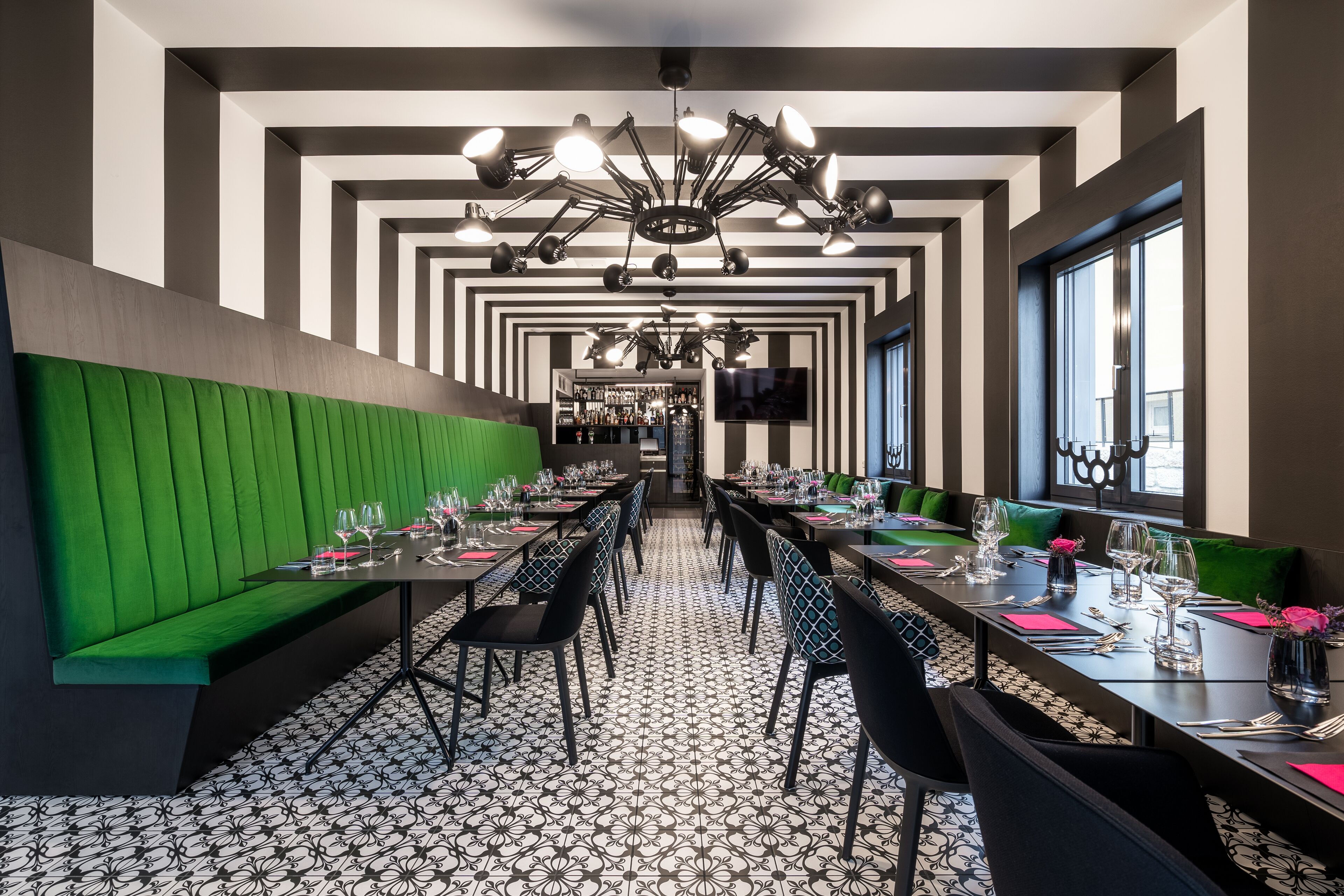 Un restaurante con un amplio salón comedor, asientos acolchados verdes y un suelo estampado.