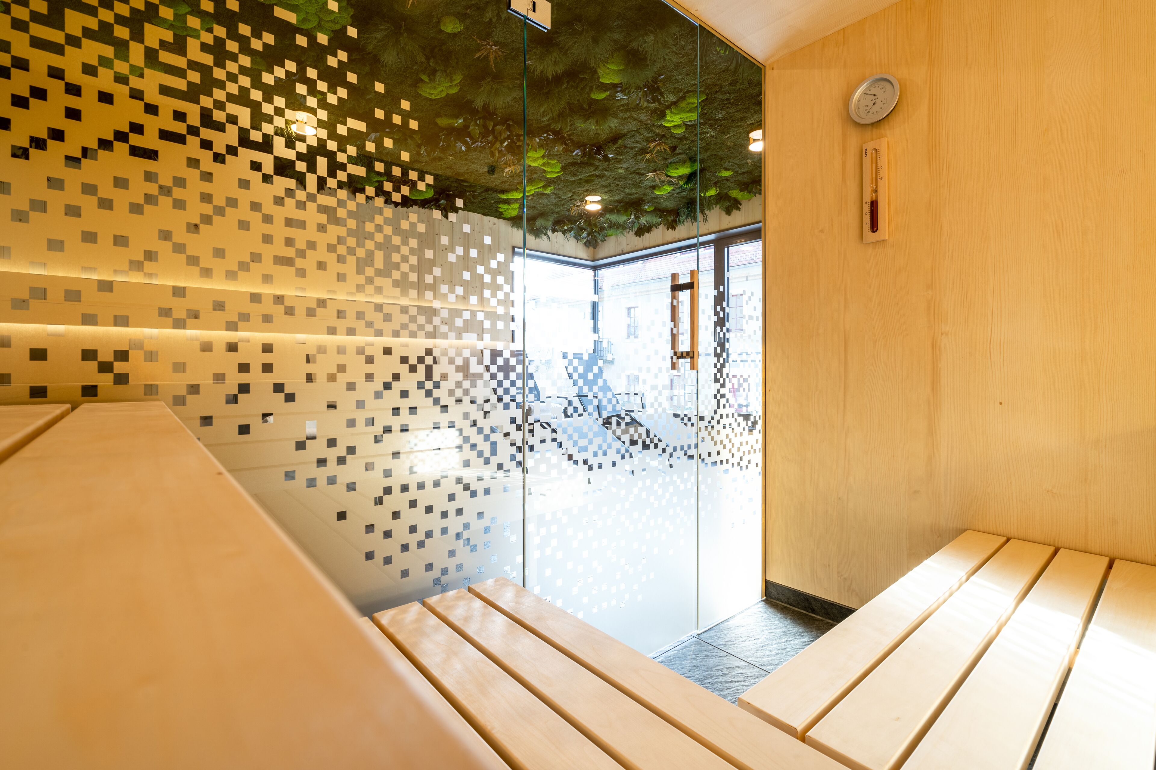 Un intérieur moderne avec des murs en verre, des bancs en bois et un plafond orné d’un motif pixélisé.
