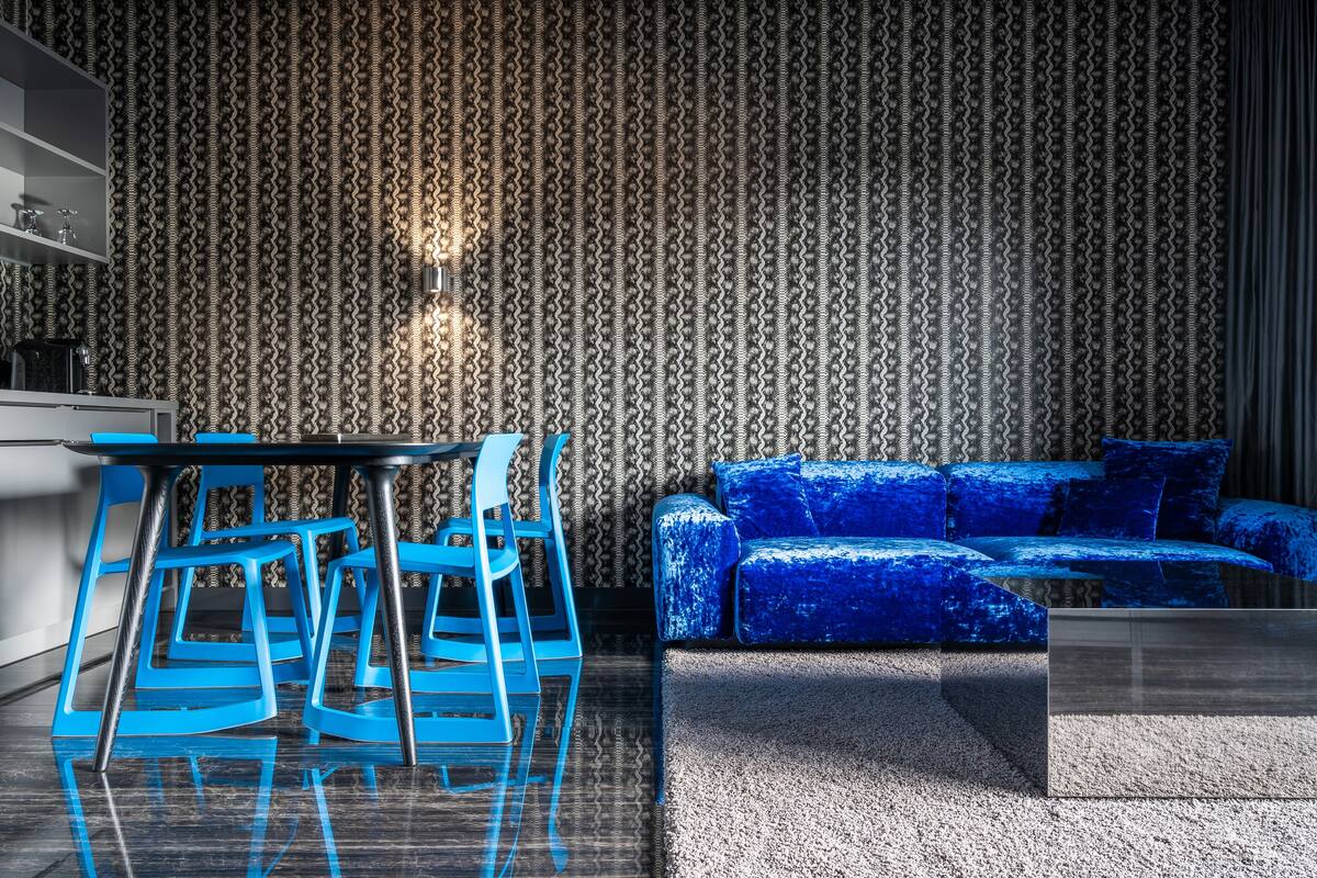 Un salon moderne avec un canapé bleu et des fauteuils assortis, une table basse en verre et un papier peint à motifs.