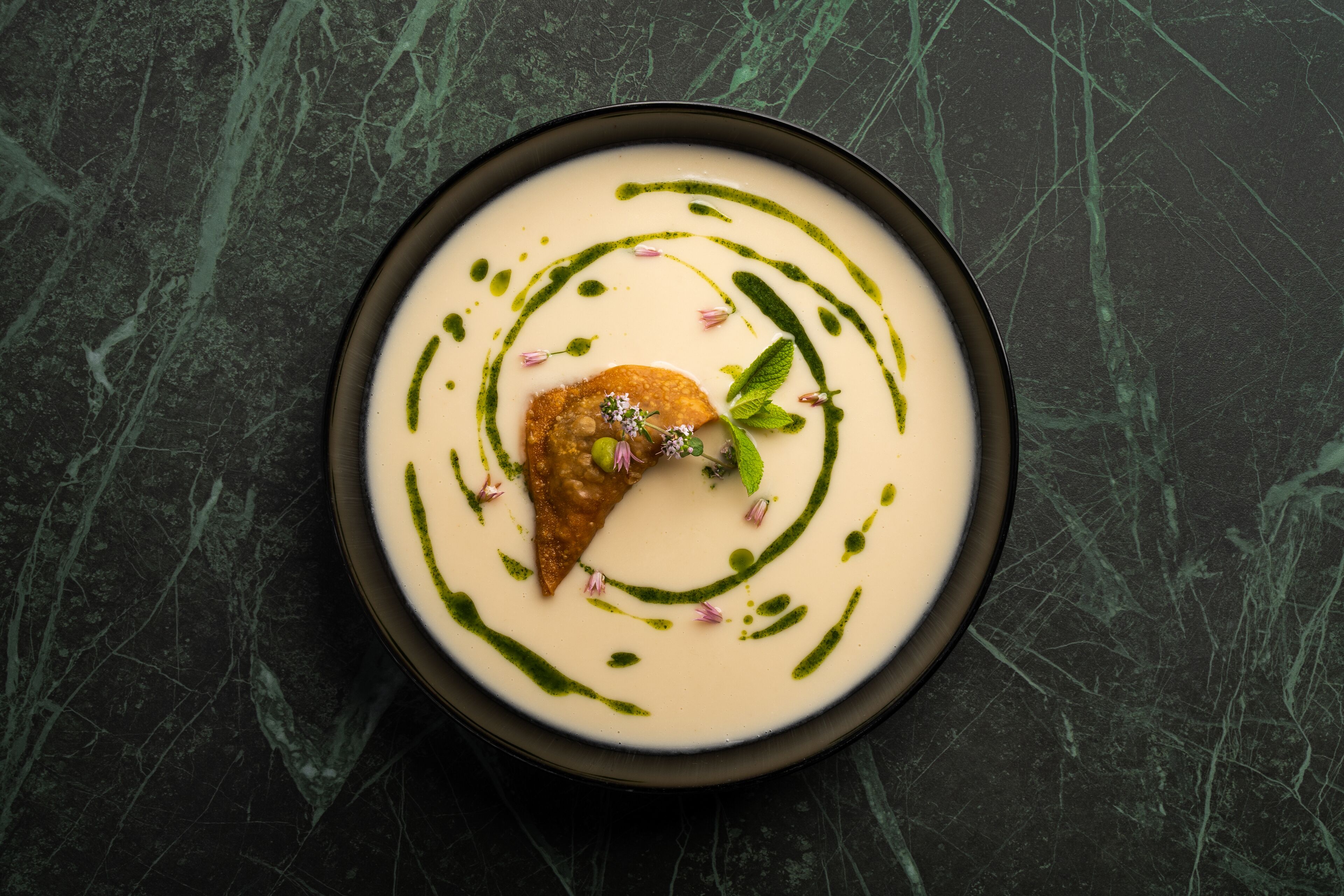 Eine Schüssel Suppe mit grüner Dekoration und einem Stück Brot auf einer dunklen Marmorplatte.
