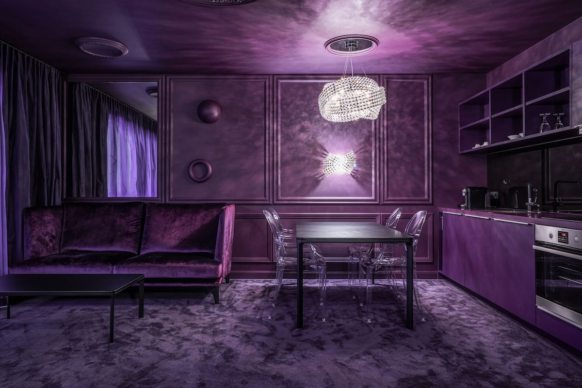 Une cuisine moderne avec un coin repas, caractérisée par une palette de couleurs violettes, un lustre et un four encastré.