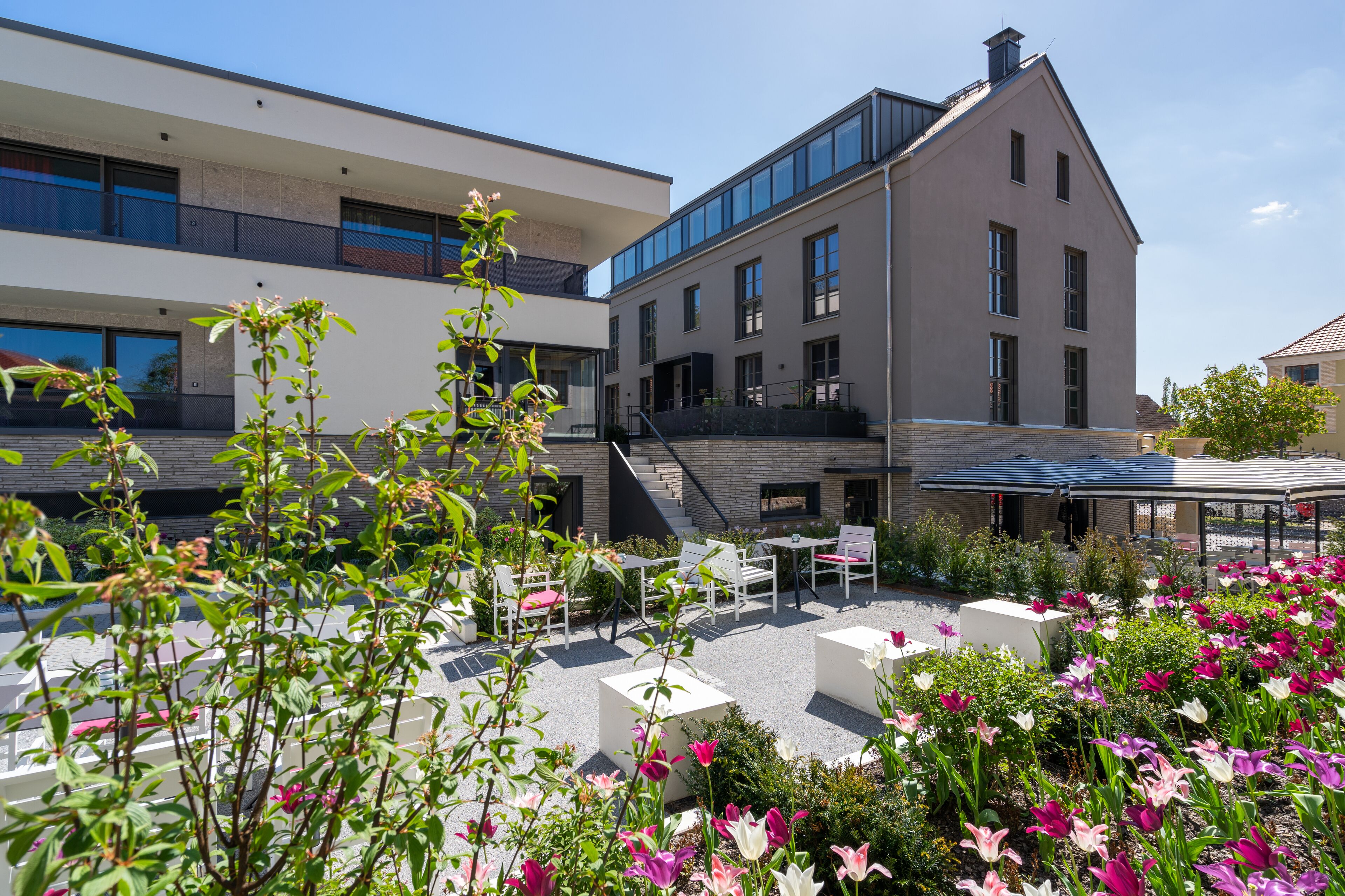 A modern building with a courtyard featuring outdoor seating and flower beds.