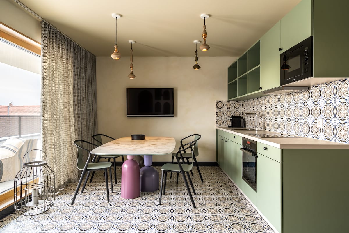Une cuisine moderne avec un coin repas, dotée d’un sol à motifs, de meubles de couleur verte, d’un four à micro-ondes et de luminaires suspendus.