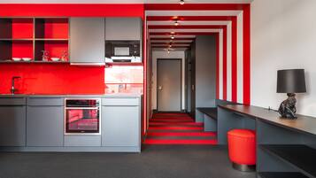 Una cocina moderna con armarios grises, una encimera roja y una escalera a rayas rojas que lleva a un pasillo.