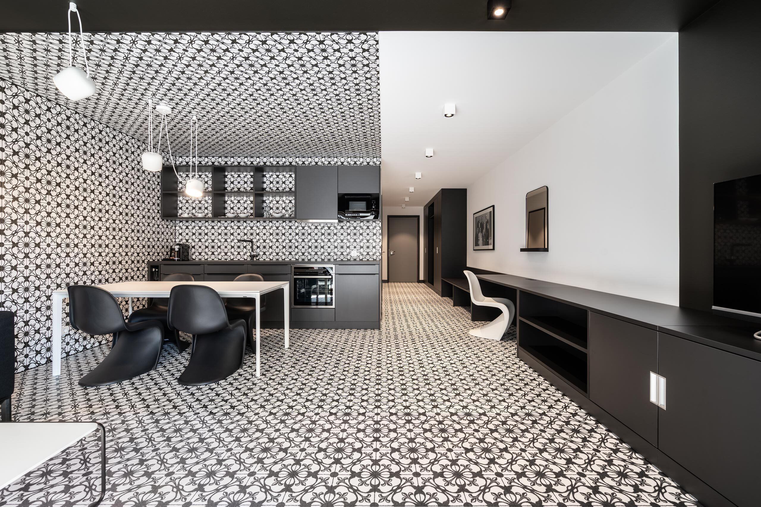 Una cocina moderna con papel tapiz estampado, una zona de comedor con sillas y un televisor sobre un mueble negro.