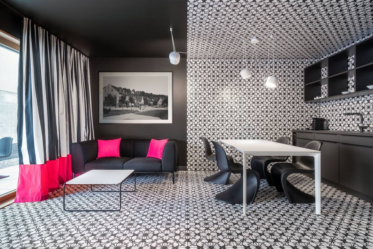 Un salon moderne avec un canapé noir, une table basse blanche et un coin repas comprenant une table blanche et des chaises noires.