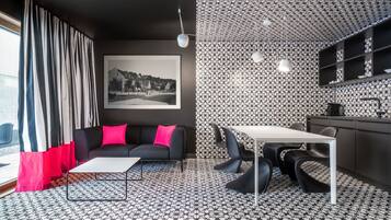 Un salon moderne avec un canapé noir, une table basse blanche et un coin repas comprenant une table blanche et des chaises noires.