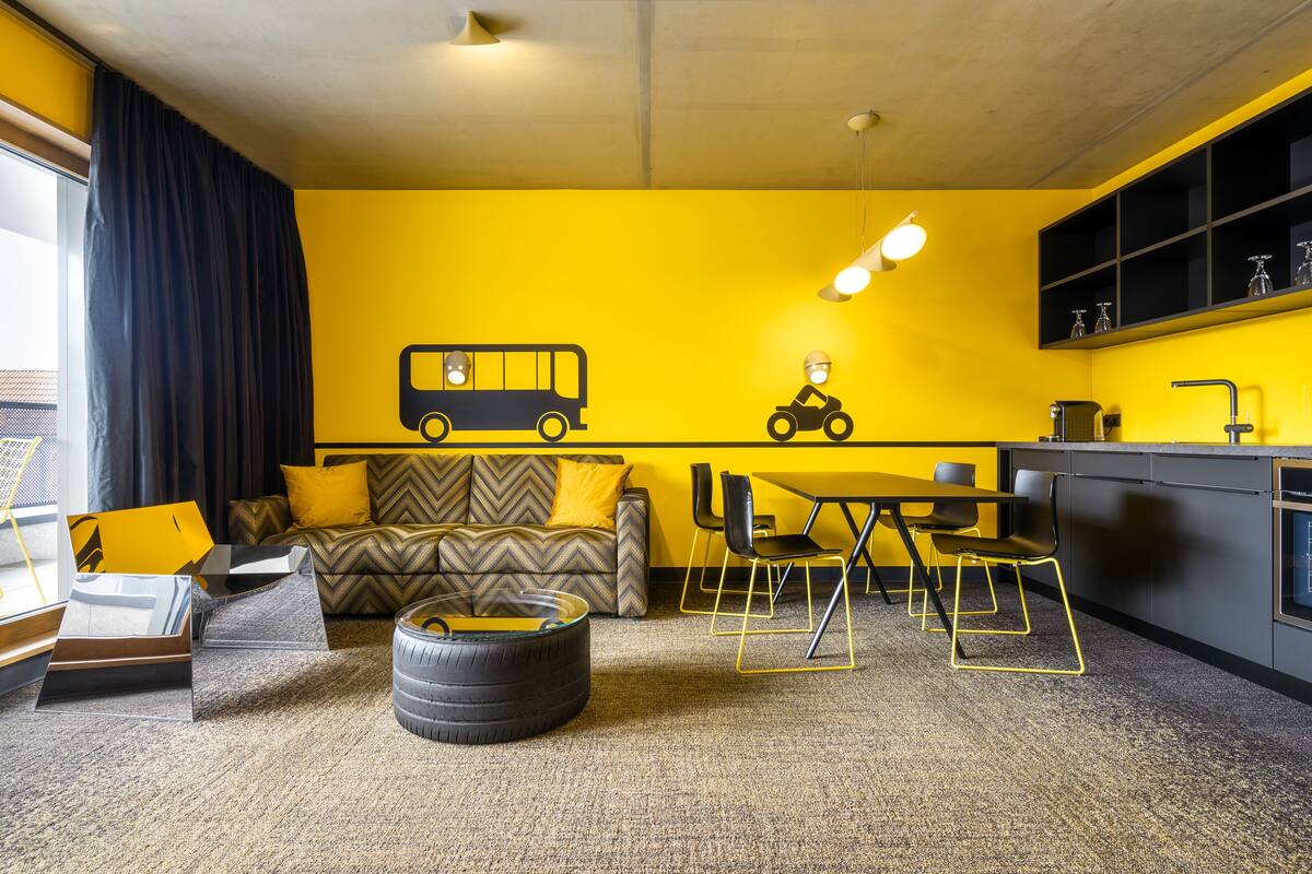 Un salon moderne avec un mur jaune, un canapé, une table basse et un coin repas avec des chaises.