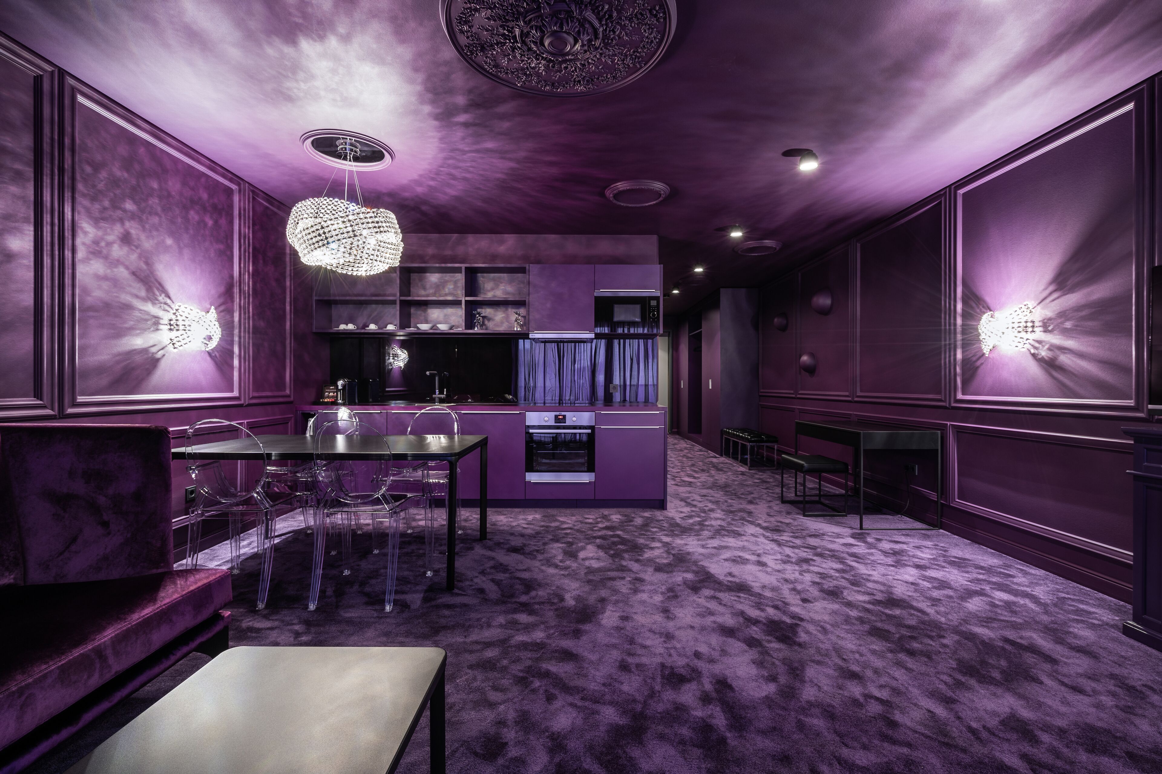 A modern interior with a purple color scheme, featuring a dining area with a table and chairs, a kitchen with a built-in oven, and a decorative ceiling light.