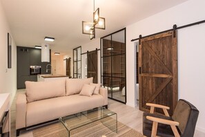 Un salon moderne avec un canapé, une table basse en verre, une chaise en bois et un placard à portes coulissantes de style grange.