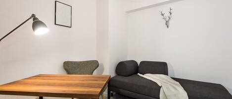 A modern, minimalist room with a wooden table, a grey sofa, and a black floor lamp.