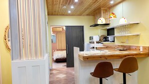 Una cocina compacta con techo de madera, un pequeño comedor con dos taburetes y un microondas en la encimera.