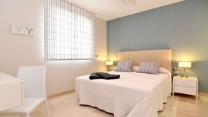Ein Hotelzimmer mit einem großen Bett, zwei Nachttischen mit Lampen, einem Sessel und einem Fenster mit Jalousien.