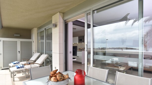 Ein moderner Außenbereich mit Sitzgelegenheiten, einem Glastisch, Liegestühlen und Blick auf den Ozean.