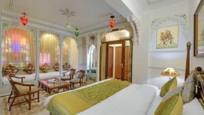 A hotel room with a large bed, a seating area with chairs, a small table, and a decorative lamp. - Hotel Raj Palace (Udaipur)