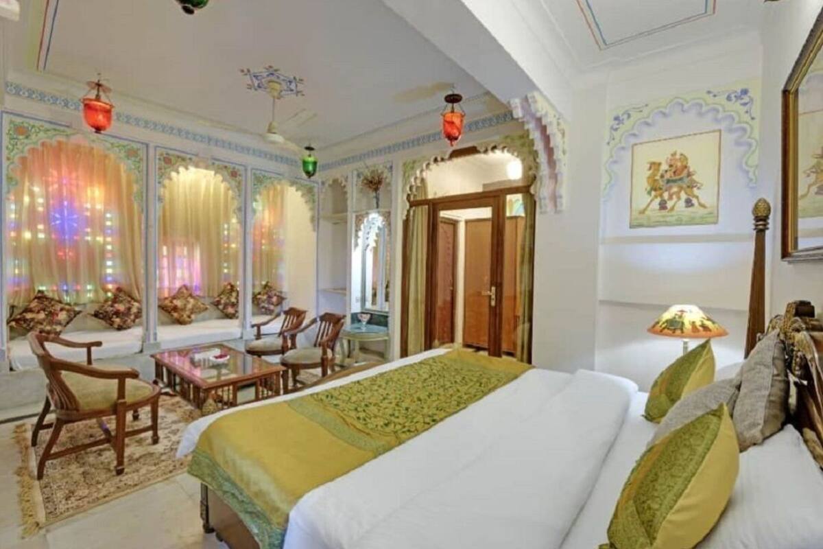 A hotel room with a large bed, a seating area with chairs, a small table, and a decorative lamp.