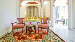A room with a bed, two chairs, a table, and a large window. - Hotel Raj Palace (Udaipur)