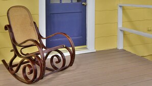 A wooden rocking chair on a porch with a blue door and yellow walls. - Coffee Klatch Cottage - Yellow (Potlatch)