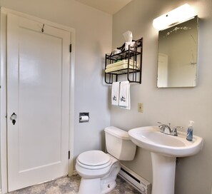 Bathroom features a toilet, sink, and mirror, along with a towel rack and storage shelf.