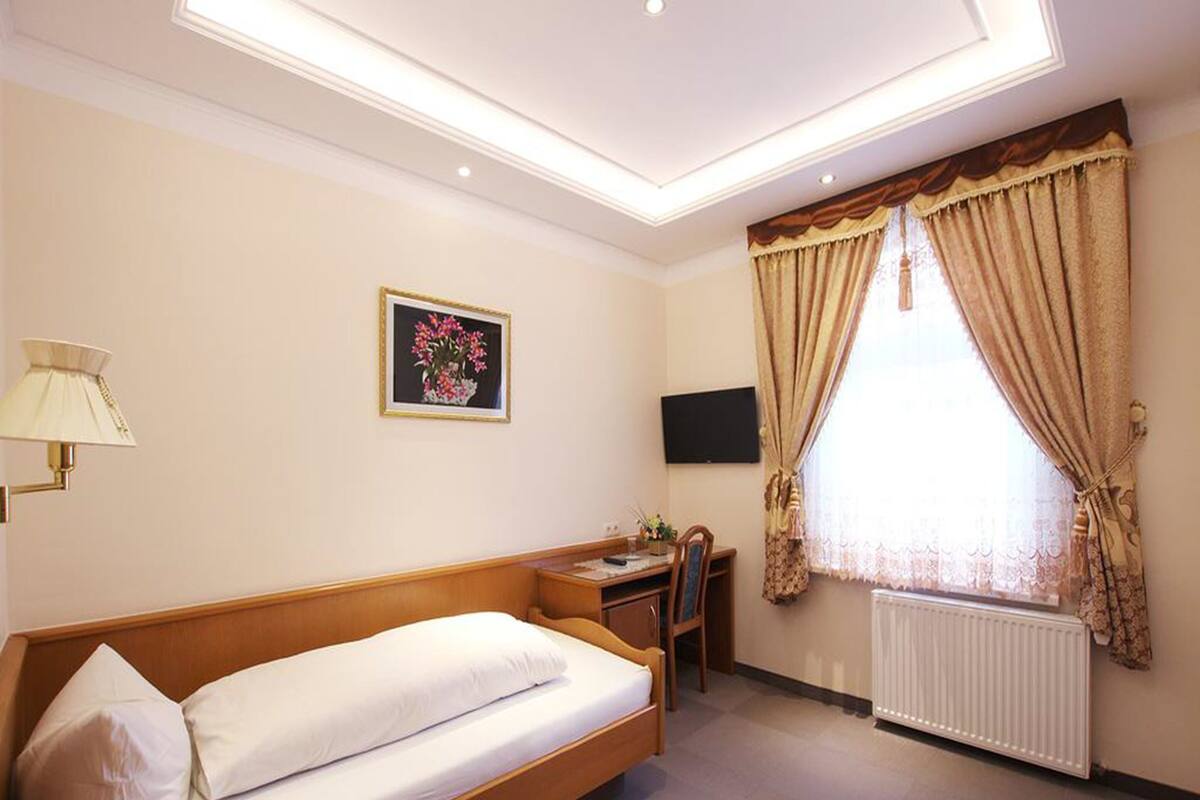 A hotel room with a bed, a desk, a chair, a TV, and a window with curtains.