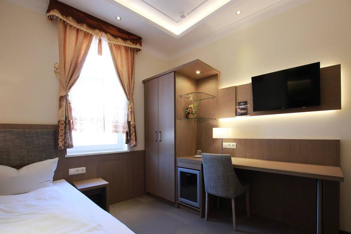 A hotel room with a bed, desk, chair, TV, and wardrobe.