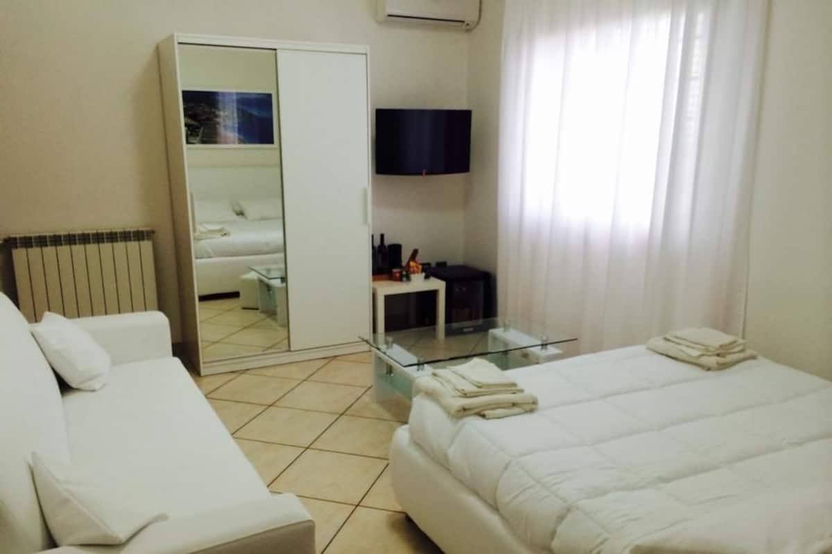 A hotel room with a bed, a sofa, a TV, and a mirror.