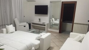 A modern hotel room with a large bed, a sitting area with a glass table, a flat-screen TV, and a bathroom visible through a glass door. - Villa Nunzia (Ercolano)