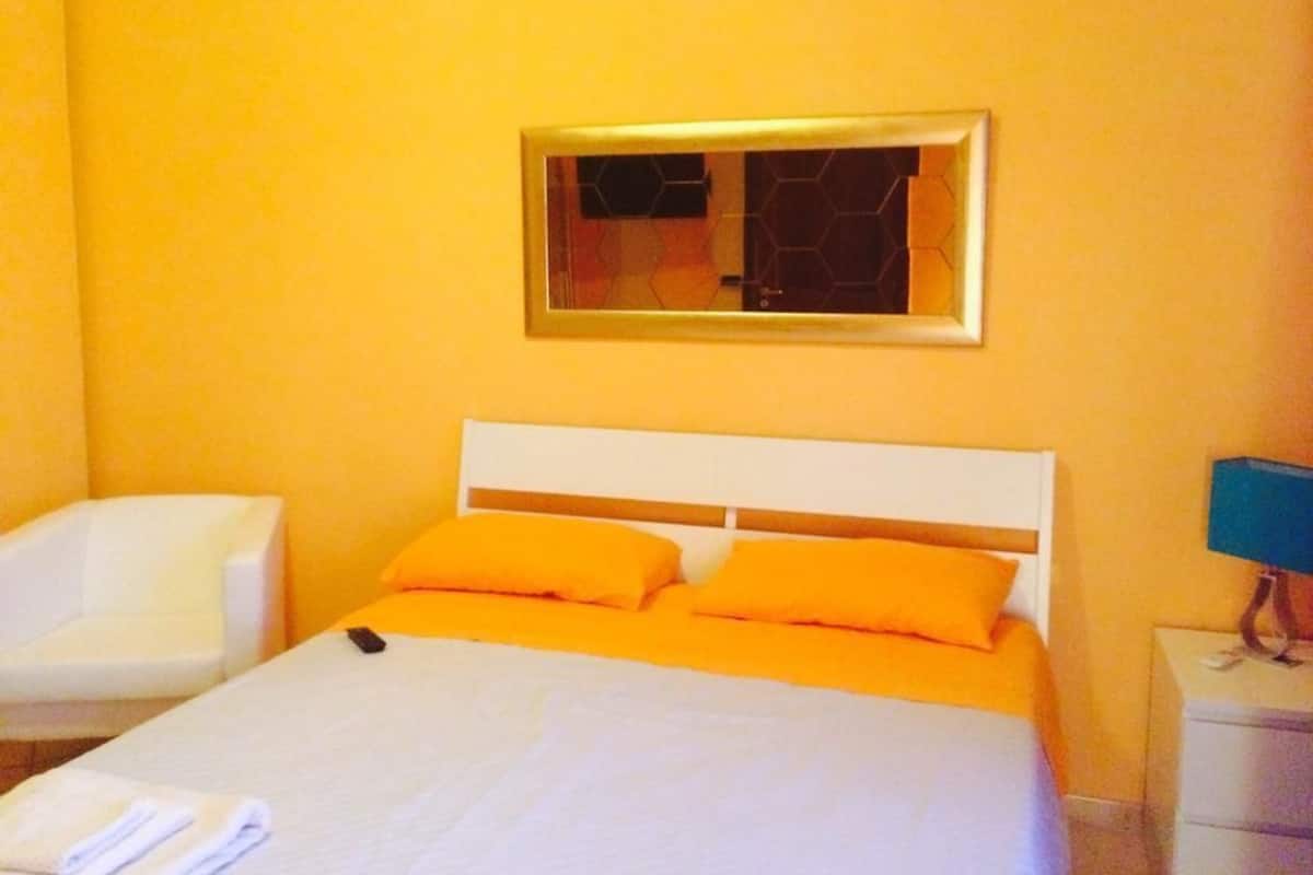 A hotel room with a bed, a chair, a nightstand, and a mirror on the wall.