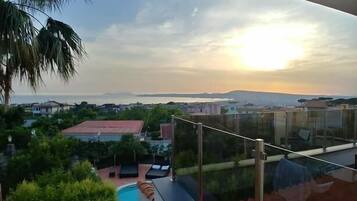 A balcony with a view of a swimming pool, palm trees, and distant buildings under a clear sky.