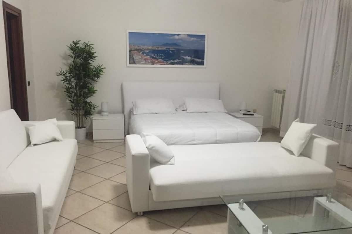 A modern hotel room with a large bed, two white sofas, a glass coffee table, and a potted plant.